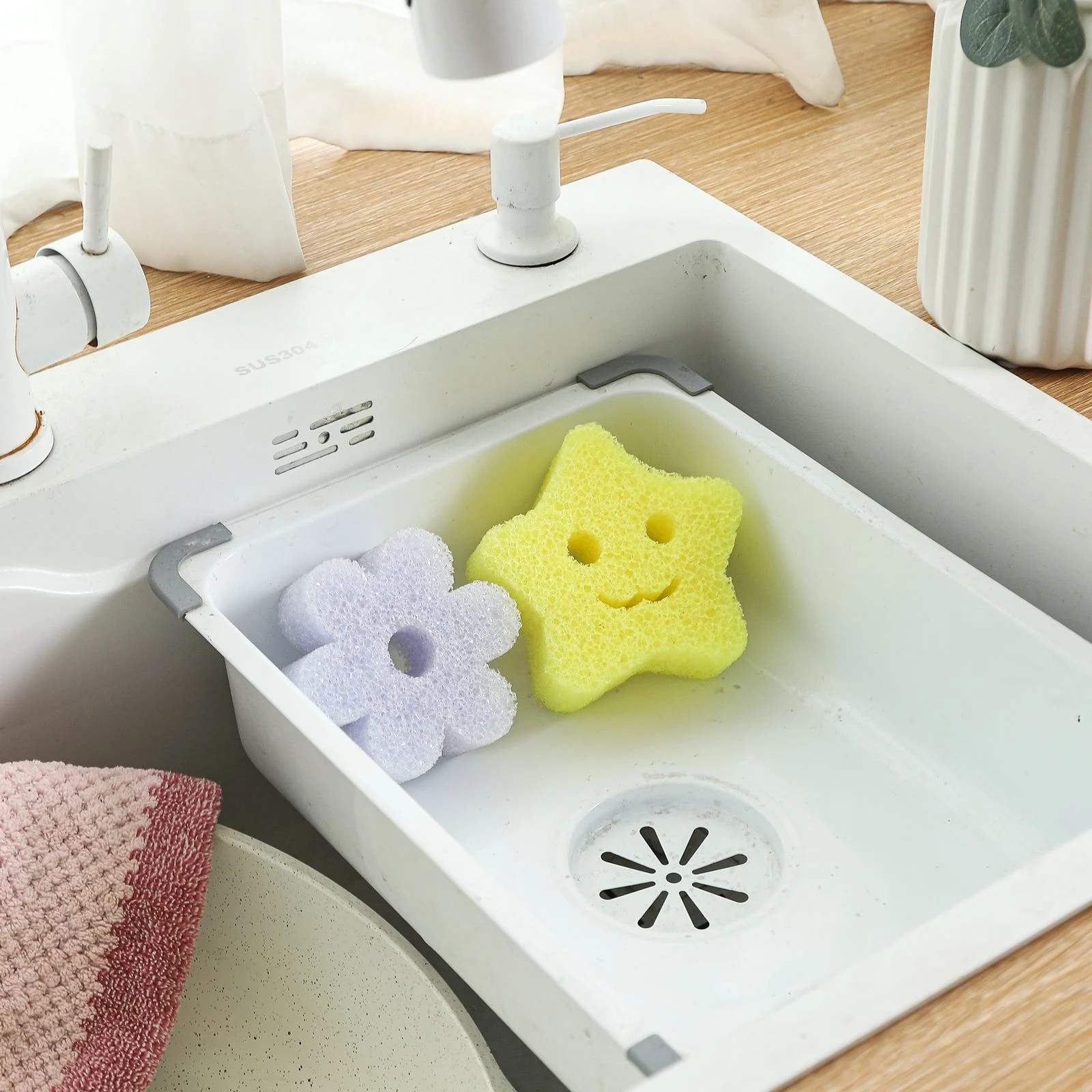 Purple flower and yellow star shaped cleaning sponges drying upright in a white sink caddy
