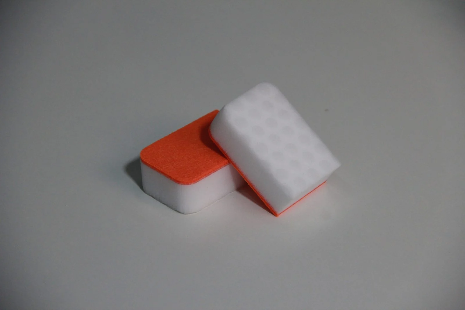 Two laminated dish sponges showing a dense white foam body with an orange scrubbing layer