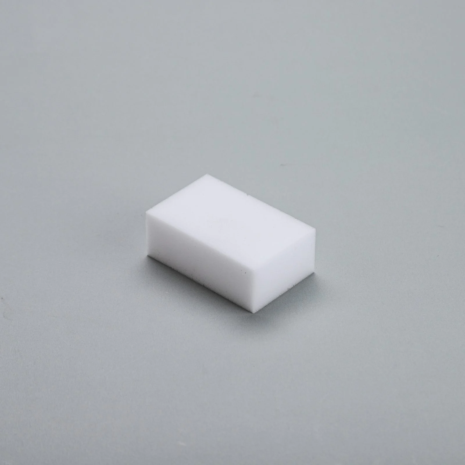 Single white melamine foam eraser sponge block photographed on a grey background