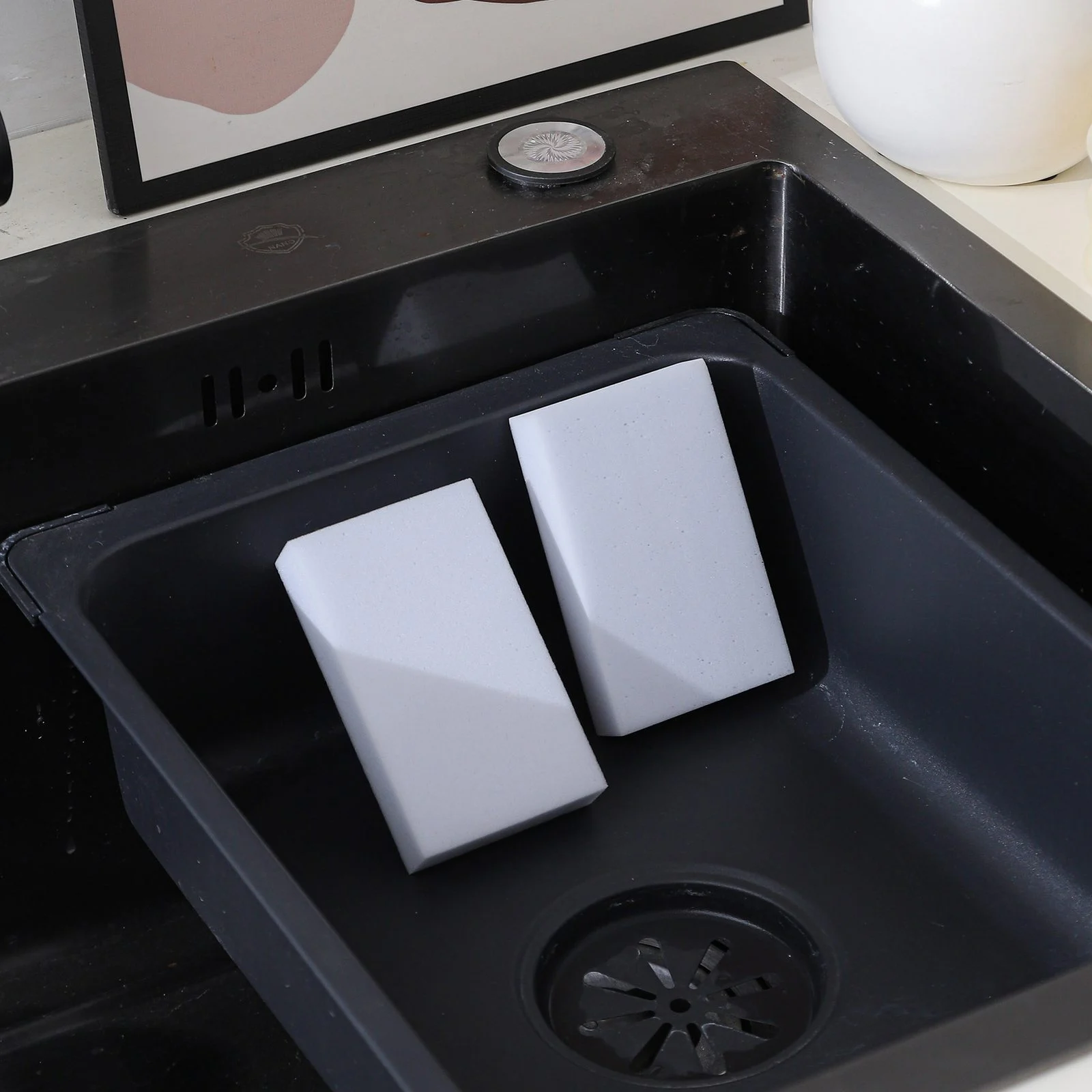 Lavender and white melamine sponge blocks resting in a dark kitchen sink